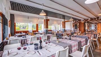 Ein Restaurant mit mehreren gedeckten Tischen, modernes Interieur und große Fenster mit Blick ins Freie.