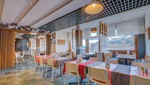 Een restaurant met meerdere tafels en stoelen, een betegelde vloer en uitzicht op buiten.