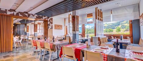 Ein Restaurant mit mehreren gedeckten Tischen, großen Fenstern mit Blick auf die Landschaft und einem modernen Interieur.