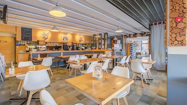 Ein modernes Restaurant mit Holztischen und weißen Stühlen, einer Bar und einer Speisekarte.