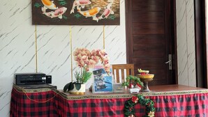 A room with a wall-mounted painting of koi fish and lotus flowers, a table with a red and black checkered tablecloth, a printer, a potted plant, a framed brochure, and a small Christmas wreath. - 12 Bedroom Villa For Group (Badung)