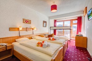 A hotel room with two beds, a desk, a chair, a TV, and a window with a view of mountains. - Hotel Relais Alpin Family Room & Balcony2 130, Les Mosses, Switzerland (Les Mosses)
