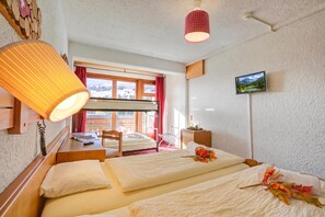 Habitación de hotel con literas, un escritorio con silla, una mesita de noche, una lámpara, un televisor y una ventana con vistas a un paisaje nevado.