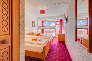 Habitación de hotel con dos camas, un escritorio, un espejo y ventana con vista a las montañas.