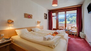 A hotel room with two beds, a table with chairs, a view of mountains, and a red curtain. - Hotel Relais Alpin Twin Room Ski In-Out 5 129, Les Mosses, Switzerland (Les Mosses)
