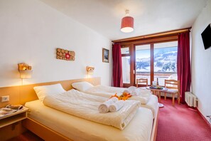 Ein Hotelzimmer mit zwei Betten, einem Fenster mit Blick auf eine verschneite Landschaft, einem kleinen Tisch mit einer Flasche und Gläsern sowie einem roten Vorhang.