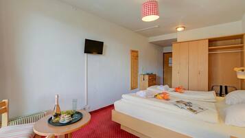 Ein Hotelzimmer mit einem Bett, einem kleinen Tisch mit einer Flasche und Gläsern, einem an der Wand befestigten Fernseher und einem Kleiderschrank.