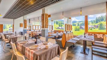 Ein Restaurant mit mehreren Tischen, Stühlen und Blick auf eine grüne Landschaft durch große Fenster.