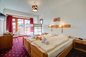Habitación de hotel con cama, escritorio, silla, televisor y ventana con vista a un paisaje nevado.