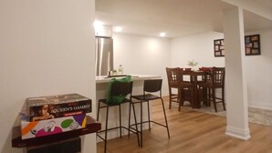 Un coin repas avec une cuisine en arrière-plan, un plancher en bois et une boîte du jeu de société « Le Gambit de la Reine » posée sur un présentoir.