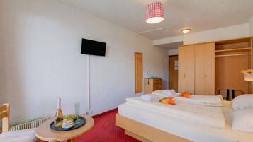 Ein Hotelzimmer mit einem Bett, einem kleinen Tisch mit Flasche und Gläsern, einem Fernseher an der Wand und einem Kleiderschrank.