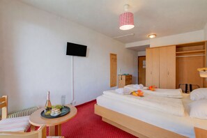 Une chambre d’hôtel avec un lit, une petite table sur laquelle se trouvent une bouteille et des verres, un téléviseur fixé au mur et une armoire.