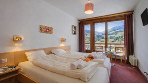 Ein Hotelzimmer mit zwei Betten, Bergblick, einem Tisch mit Stuhl und einem kleinen Balkon.