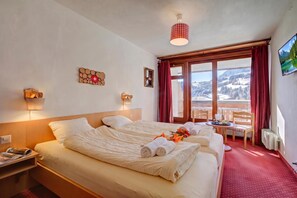 Una habitación de hotel con cama, mesitas de noche, ventana con vistas y una mesa con toallas y vasos.
