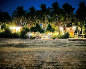 Ein Anwesen direkt am Strand mit Sand, Palmen und einem Gebäude mit beleuchteten Fenstern.