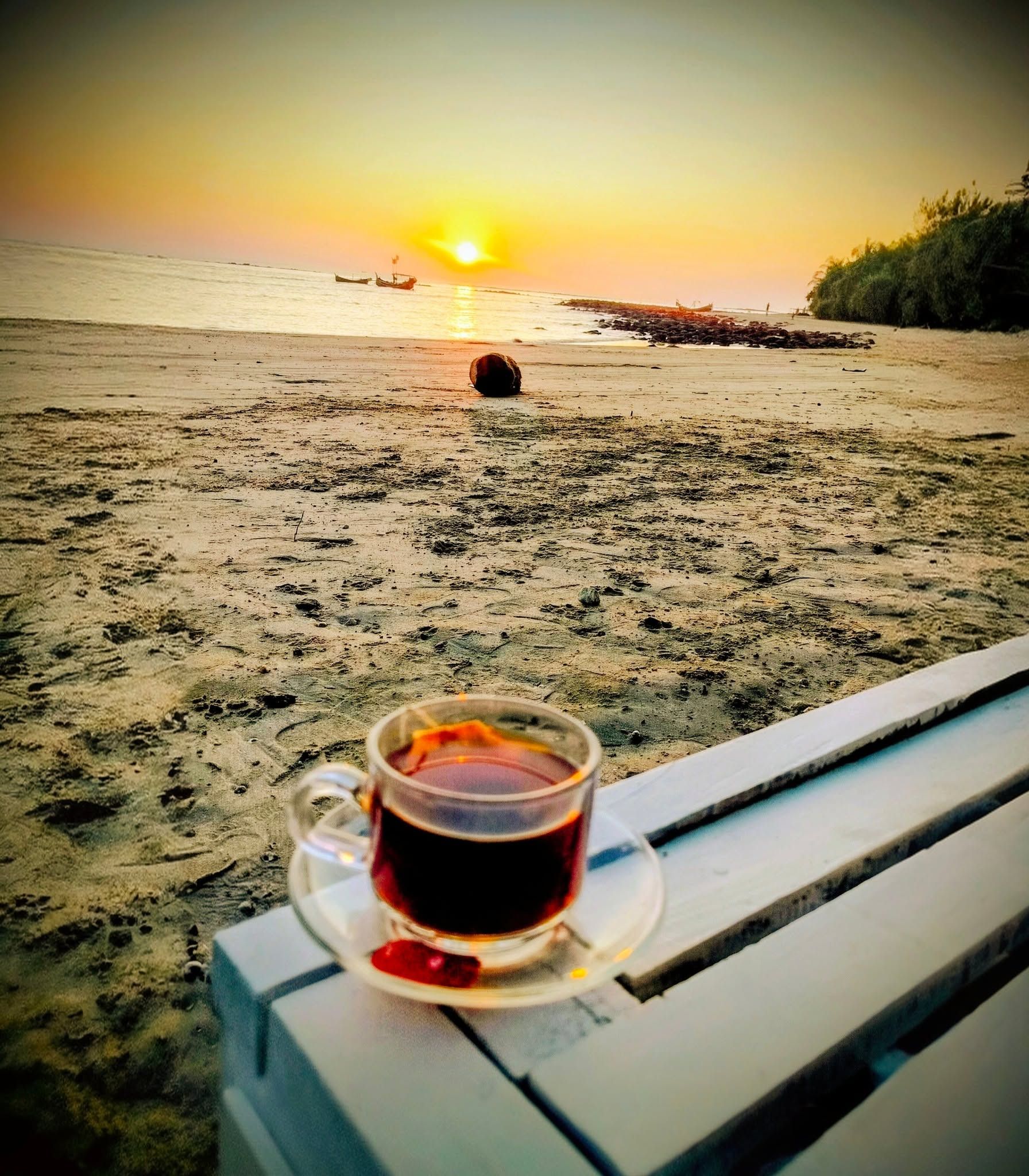 Una tassa de cafè sobre una banca amb vista a una platja al capvespre.