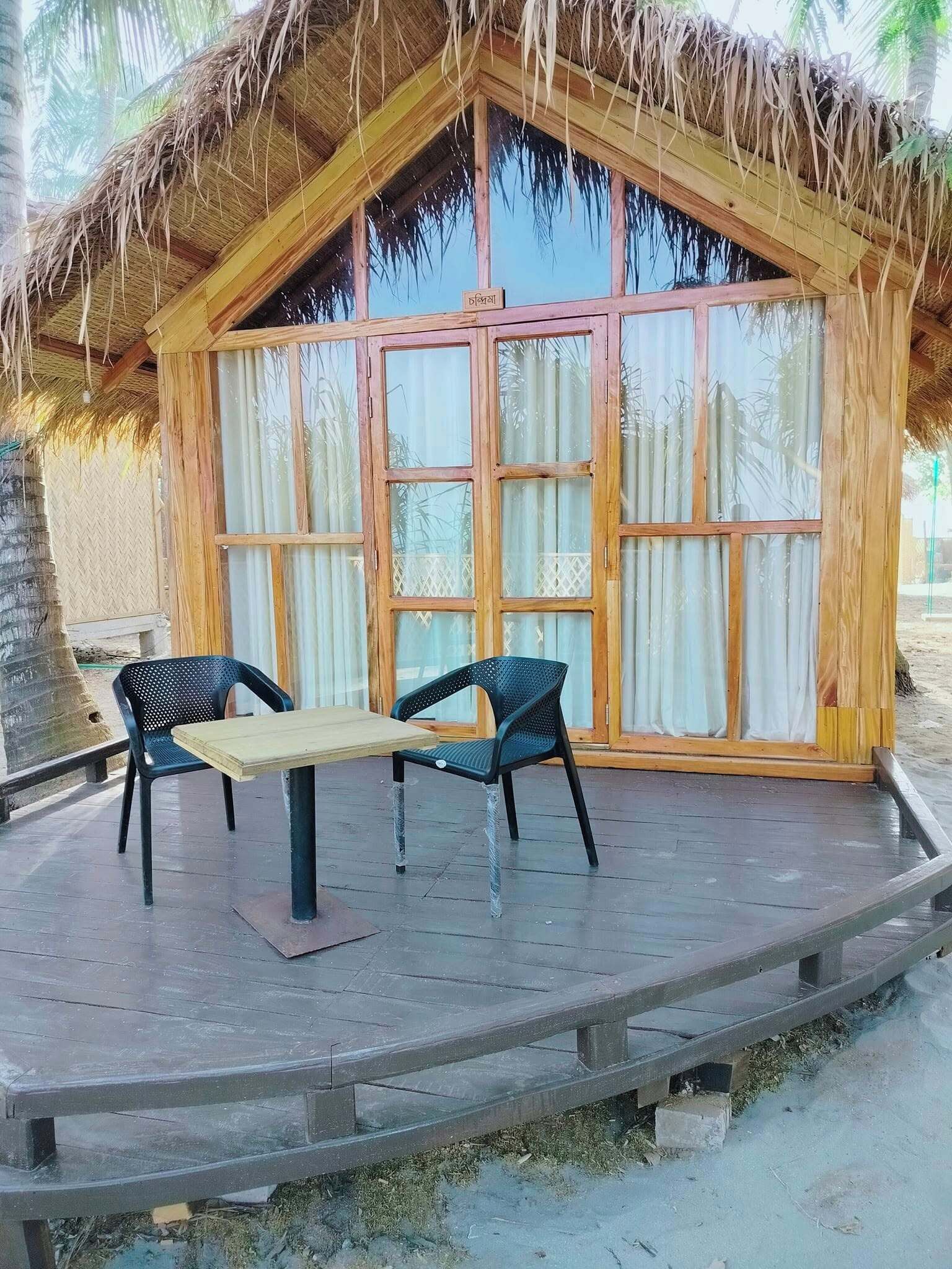 Une structure en bois avec un toit de chaume, deux chaises et une table sur une terrasse en bois.