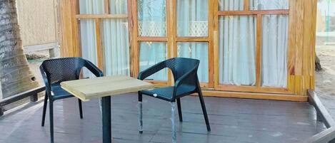 Une structure en bois avec un toit de chaume, deux chaises et une table sur une terrasse en bois.