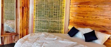 A wooden cabin bedroom with a large bed, a mirror, and a woven wall panel.
