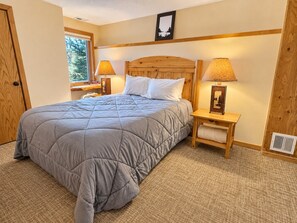 Un dormitorio con una cama grande, dos mesitas de noche con lámparas, un cabecero de madera y una ventana con vista a árboles.