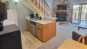 Una cucina con lavastoviglie, piano cottura e lavello. C'è una zona pranzo con tavolo e sedie. Una scala conduce al secondo piano.