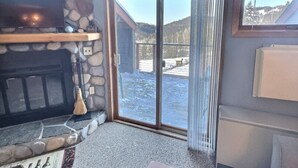 Un camino in pietra con una televisione sopra, una porta vetrata scorrevole che dà su una zona esterna innevata e vista su una montagna.