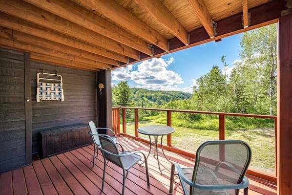 A wooden deck with two chairs and a small table, overlooking a scenic landscape.