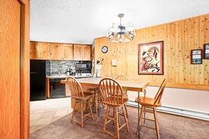 A kitchen with wooden cabinets, a black refrigerator, a microwave, and a dining area with a wooden table and chairs.