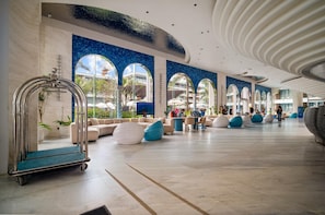 Eine großzügige Lobby mit modernem Design, ausgestattet mit einer gemütlichen Sitzecke, einem Servicewagen und Blick ins Freie durch große Fenster.