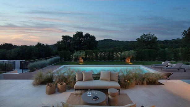 Ein stilvoller Außenbereich mit einer Sitzecke, einer Couch und Sesseln, einem runden Tisch und einem Pool im Hintergrund.