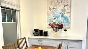 A dining area with a wooden table, four chairs, a vase with flowers, a coffee maker, a toaster, and a framed floral artwork on the wall. - Private Entire Guest Suite, 1 min to bus stops to Downtown and many attractions. (Vancouver)