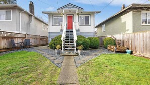 A two-story house with a red door, a front porch, and a small staircase leading to the entrance. - Private Entire Guest Suite, 1 min to bus stops to Downtown and many attractions. (Vancouver)