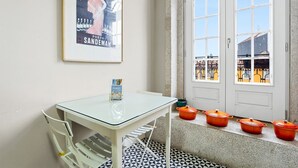 Una stanza con un tavolo in vetro, un poster incorniciato, una porta con vetrate e vasi arancioni sul davanzale.
