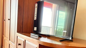 A wooden cabinet with a flat-screen TV on top, a vase on a shelf, and a remote control on the cabinet. - Sunset Ocean View 3-king bed Villa Directly Above Patong (Phuket)