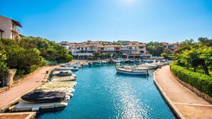 A marina with boats docked, a clear blue sky, and buildings in the background. - La Terrazza Segreta (Olbia)