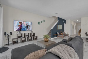 A modern living room with a large flat-screen TV, a staircase, and a dining area. - Three Themed Worlds. One Unforgettable Family Stay. (Kissimmee)