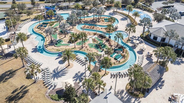 An aerial view of a resort with a winding pool, palm trees, and a beach area. - Three Themed Worlds. One Unforgettable Family Stay. (Kissimmee)