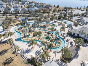 Vista aèria d'un complex turístic amb una piscina sinuosa, palmeres i una zona de platja.