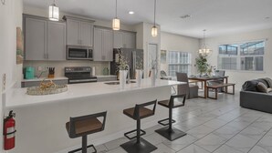 A modern kitchen with a large island, bar stools, and pendant lighting. - Three Themed Worlds. One Unforgettable Family Stay. (Kissimmee)