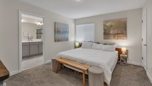 A bedroom with a large bed, a wooden bench, a nightstand, and a painting on the wall. - Three Themed Worlds. One Unforgettable Family Stay. (Kissimmee)