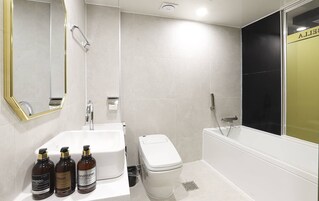 Un baño moderno con lavamanos, inodoro y bañera blancos. Hay tres botellas de champú, acondicionador y gel de baño sobre el mostrador.