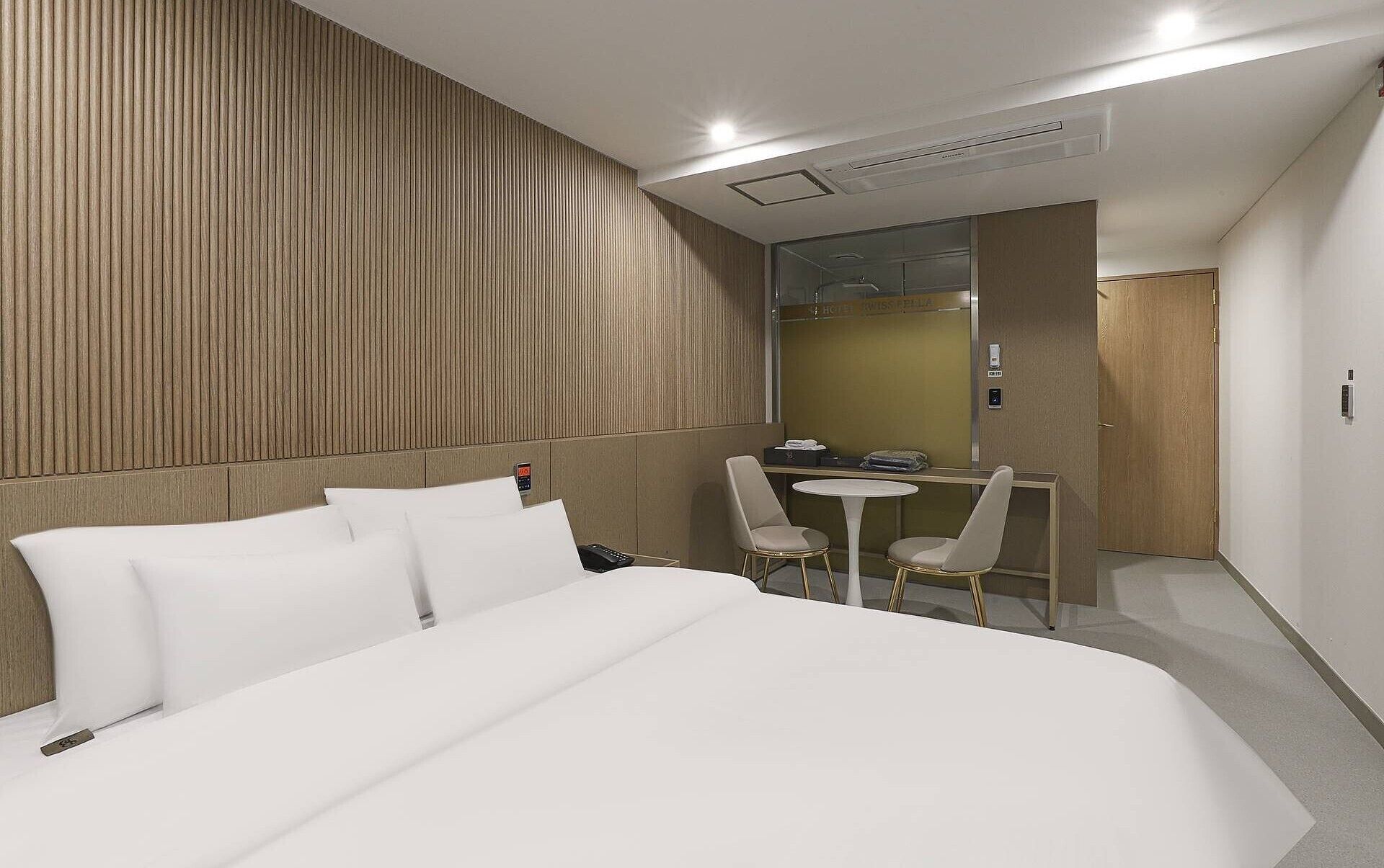 A hotel room with a bed, a desk, two chairs, a mirror, and a door.