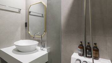 Un baño moderno con un lavamanos blanco, un espejo con marco dorado y una ducha con manguera. Hay tres botellas de artículos de tocador en la pared.