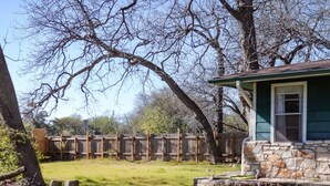 A stone house with a green roof, surrounded by a wooden fence and trees. - Stylish Musician`s Flat With Creekside Garden (Austin)