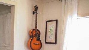 A dining area with a round table, two chairs, a guitar, a framed picture, and a vase with flowers. - Stylish Musician`s Flat With Creekside Garden (Austin)