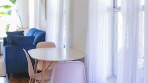 Huone, jossa on ruokapöytä, tuoleja, sininen sohva ja ikkuna, jossa on läpikuultavat verhot.