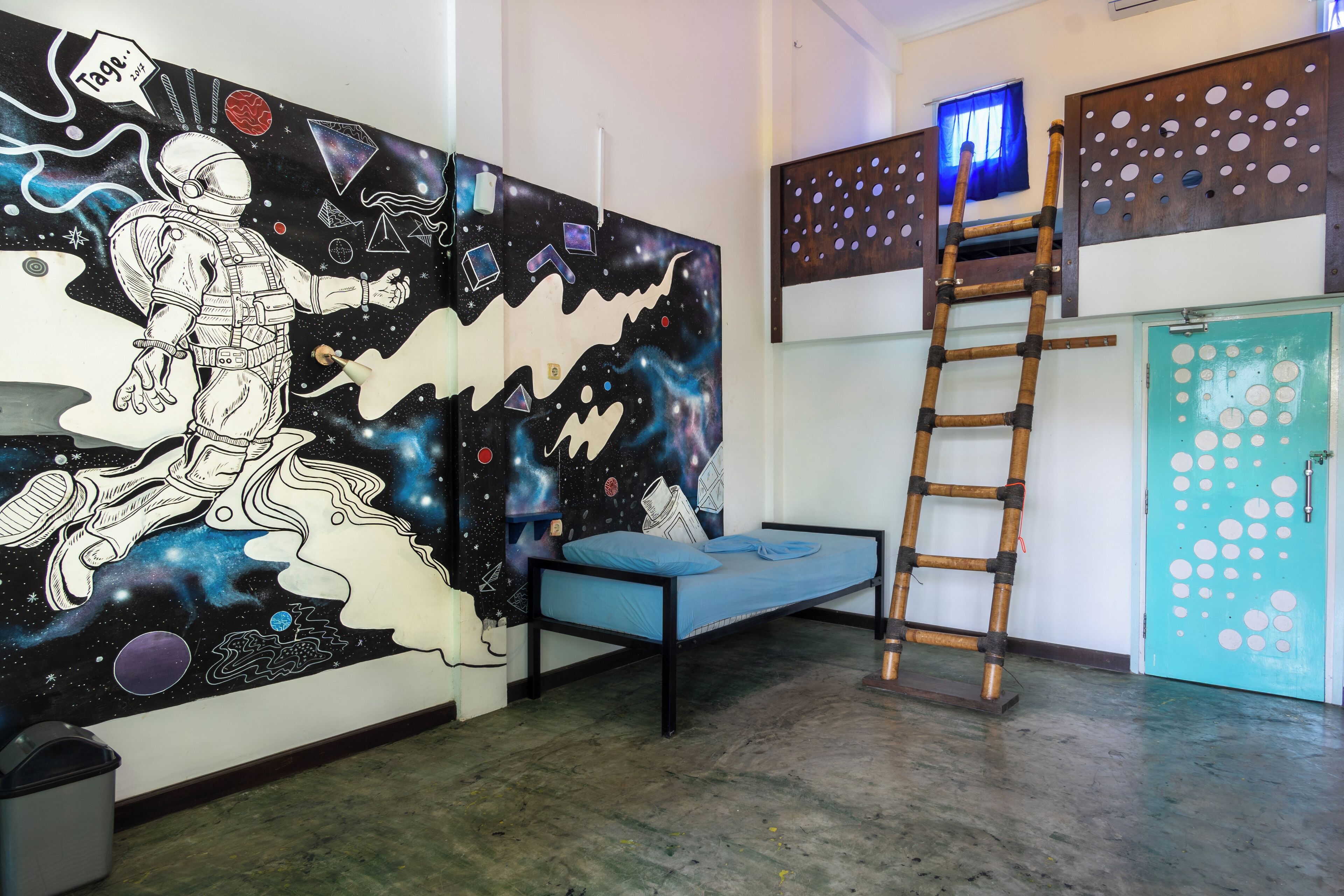 A room with a bed, a ladder, a wall mural, and a door with circular cutouts.