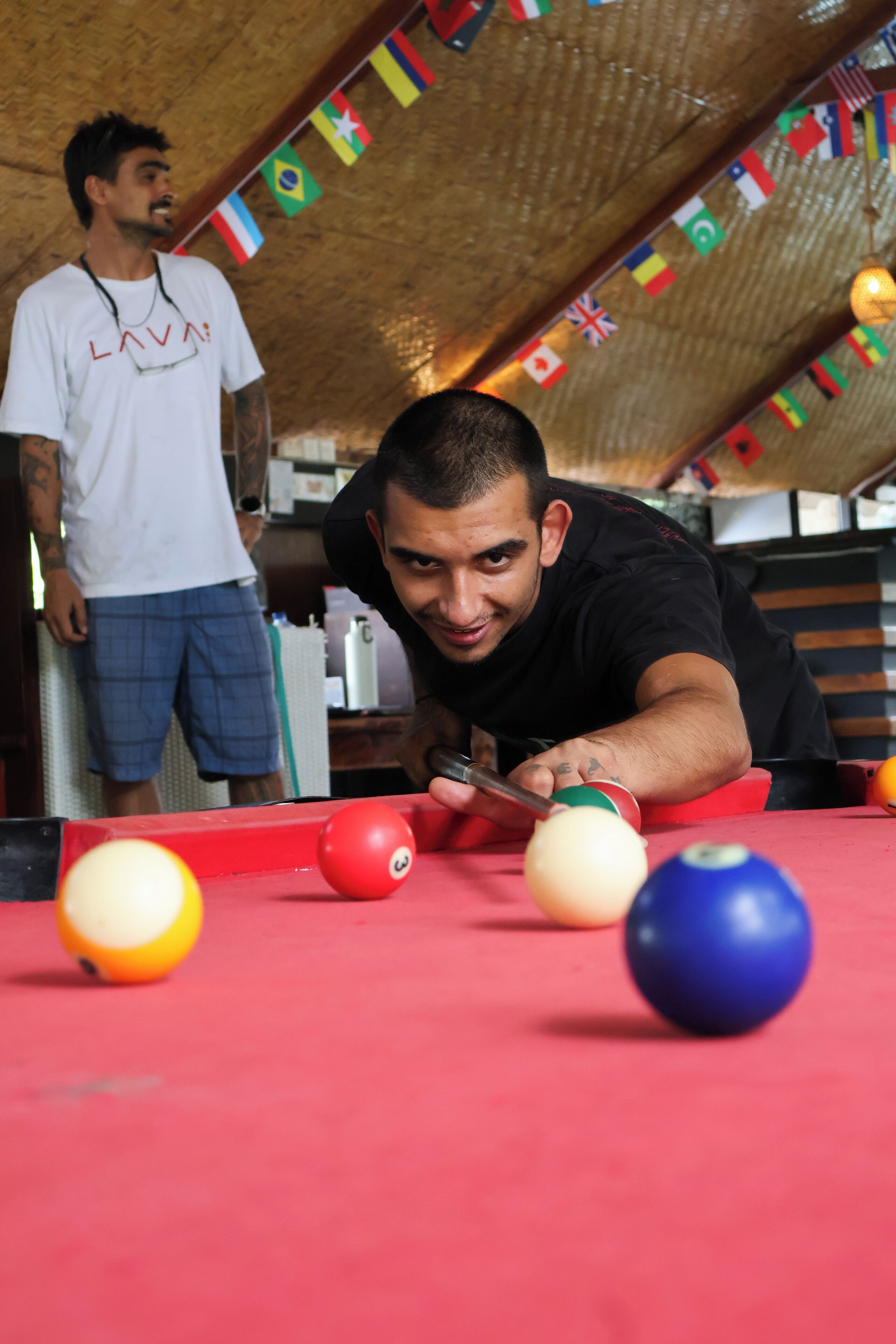 A pool table with balls and a person playing. Flags are visible in the background.