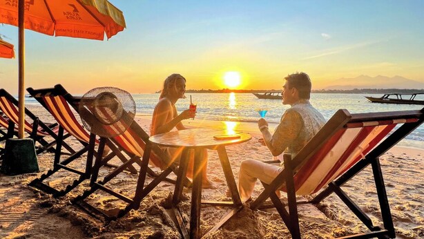 Mesa y sillas con sombrillas frente a la playa, con vista al mar y al atardecer.