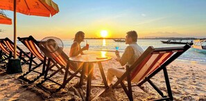 Mesa y sillas con sombrillas frente a la playa, con vista al mar y al atardecer.
